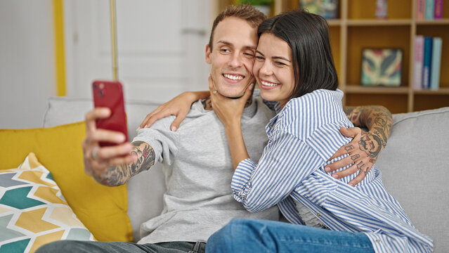 Beautiful couple sitting on sofa together taking selfie picture by smartphone at home