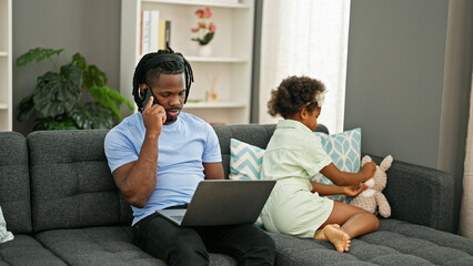 African american father and daughter sitting on sofa working and playing at home