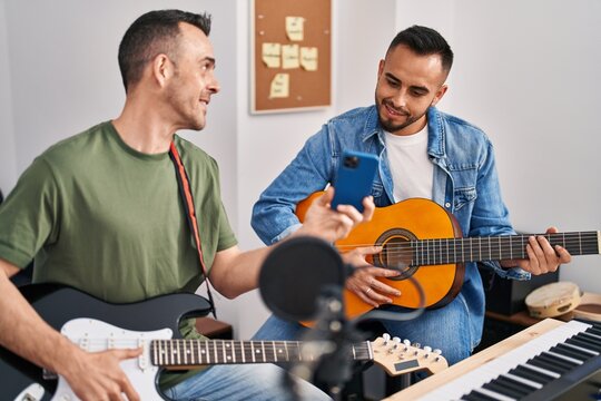 Two men musicians playing classical and electrical guitar looking smartphone screen at music studio