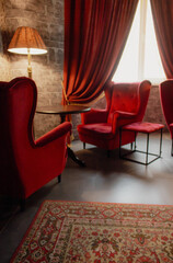 Red armchairs and table with lamp in cozy classic interior. Antique living room with red curtains...