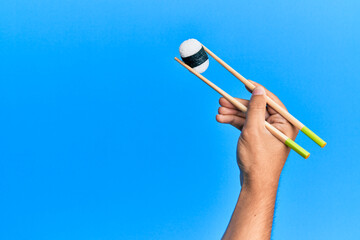  Hand of man holding sushi with chopsticks over isolated blue background
