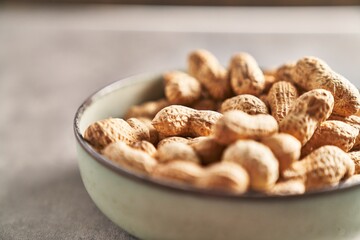 Obraz na płótnie Canvas Close-up of unshelled peanuts in a bowl on a textured tabletop, hinting at healthy snacking.
