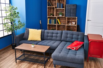A cozy modern living room with a blue sectional sofa, wooden shelves, a red cabinet, and a potted plant beside a bright window.