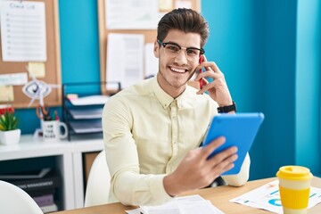 Young hispanic man business worker talking on smartphone using touchpad at office