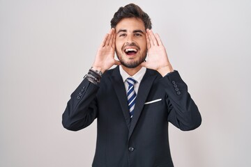Young hispanic man with tattoos wearing business suit and tie smiling cheerful playing peek a boo...