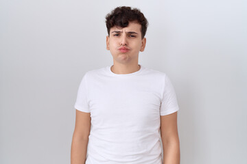 Young non binary man wearing casual white t shirt puffing cheeks with funny face. mouth inflated with air, crazy expression.