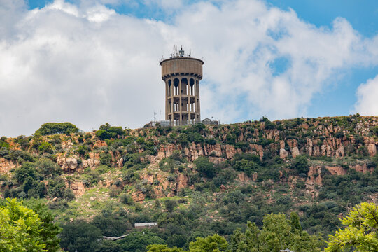 View of Northcliff Water tower reservoir from directly below in between the trees. Clear, bright day with some light clouds against a blue sky.