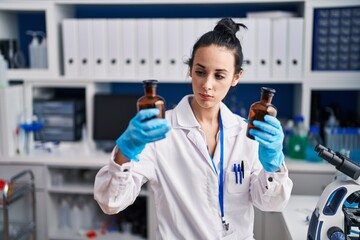 Young caucasian woman scientist holding bottles at laboratory