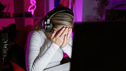 Stressed woman in headphones faces gaming computer in a dark room with colorful neon light. © Krakenimages.com