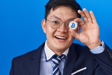 Young asian man holding virtual currency bitcoin covering eye celebrating crazy and amazed for success with open eyes screaming excited.