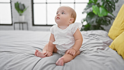 Adorable baby, a little toddler in comfy clothes, sitting relaxed on the bed sheet with a serious face in the morning! indoor lifestyle in the infant's room that exudes comfort and relaxation