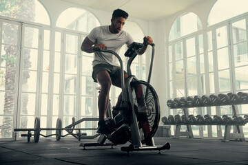 Athletic young multiracial man in sports clothing cycling on exercise bike at the gym