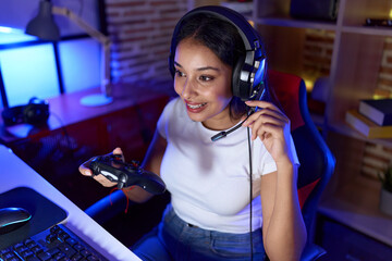 Young arab woman streamer playing video game using joystick at gaming room