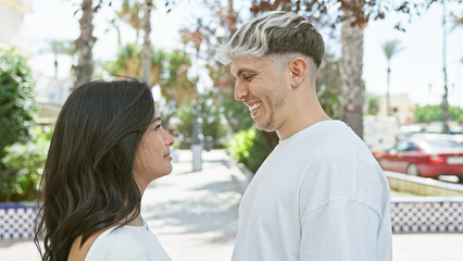 Obraz premium A loving couple stands together outdoors, surrounded by greenery and urban elements.