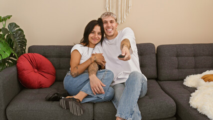 A cheerful couple sitting together on a sofa in a cozy living room, with the man holding a remote control.