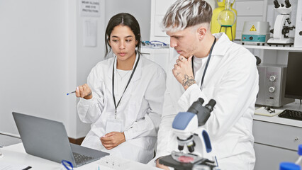 A woman and man scientist in a laboratory analyzing data on a laptop together.