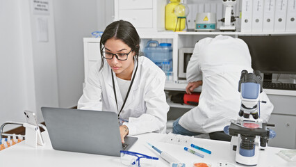 Woman and man scientists researching in laboratory with microscope, computer, and lab equipment