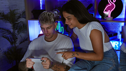 A young man and woman enjoy a casual gaming session in a neon-lit room at night, embodying contemporary leisure.