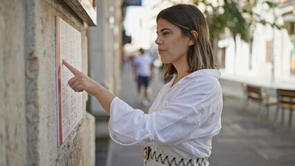 Young beautiful hispanic woman reading restaurant menu at the street
