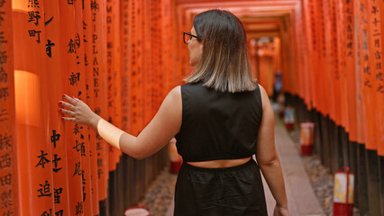Captivating view of a beautiful hispanic woman in glasses, lost in the mesmerizing walk through the vibrant orange torii gates at fushimi, embodying the essence of traditional japanese culture.