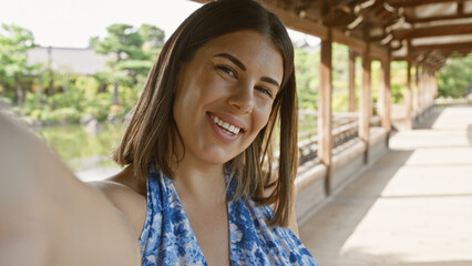 Confident hispanic woman, an all-smile beautiful brunette, enjoys taking a fun selfie at...