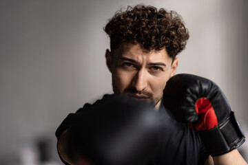 Boxer with red boxing gloves training with a punch bag in a room