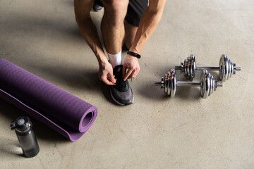 Close up of man in fitness clothing fastening trainers before exercising with hand weights at home