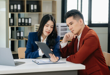 Fototapeta premium Asian business colleague business presents and explains and using laptop and tablet. Teamwork, financial marketing team, while sitting in modern office