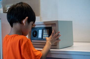 Little Asian boy opening safe at home