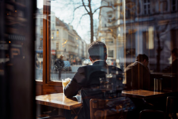 Obraz premium A man in a suit sits at a table in a cafe, looking out the window.