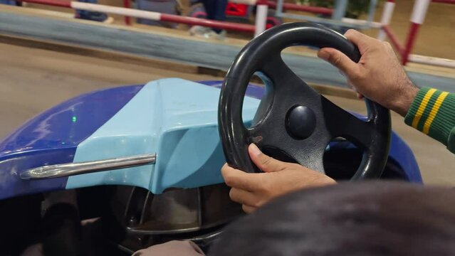 closeup man hand on a bumper car steering wheel with colorful cars in the background at an amusement park