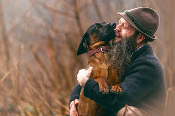 A bavarian man wearing a traditional folk costume interacting with his bavarian mountain dog nearby - obrazy, fototapety, plakaty