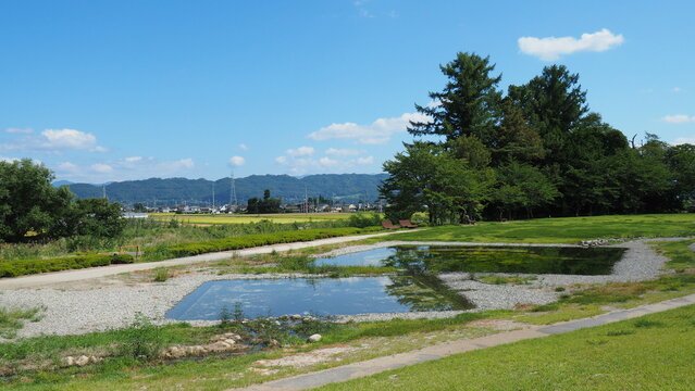 Outdoor area near Chihiro Art Museum in Azumino, ponds of water reflecting the blue sky, green trees and grassland, with Japanese village in the further background