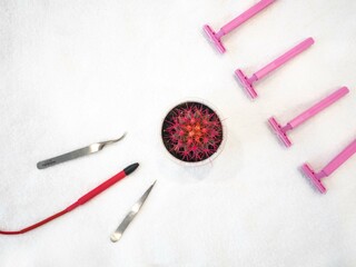 A cactus with pink needles, tweezers, an electric hair removal pen and shaving machines on a white terry towel. The concept of removing unwanted hair is epilation. View from above