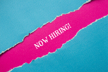 Now hiring words written on blue torn paper with pink background. Conceptual business symbol. Copy...