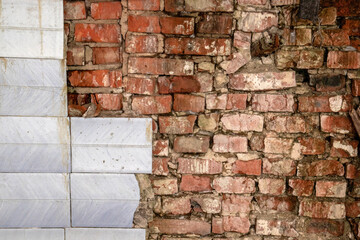 The bricks are stacked crookedly on the wall. Brickwork with a fragment of facing tile. Bricks of different shades on the wall with parts of ceramic cladding.