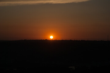 A serene sunset with a radiant sun dipping below the horizon, casting a warm glow over the landscape