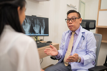Mature male doctor explain to the woman patient the result of x-ray that show fracture of her calcaneus. Doctor Showing X-ray To Patient On Computer Screen.