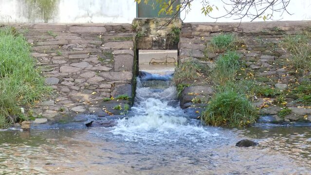 Flow of river water overflowed by the rains, surpassing a gate of a small dam in an irrigation canal