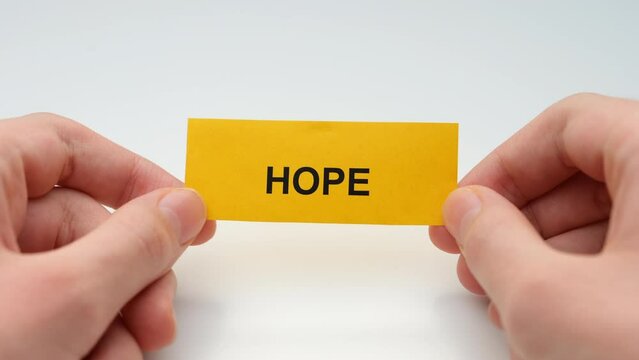 A young man holding a yellow paper note with the word Hope on it in his hands. Close up.