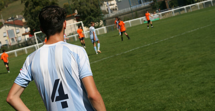 Des  jeunes joueurs de football sur un terrain pendant un match, vue de dos, image avec espace pour texte.