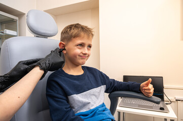 little boy, fair-haired teenager, sitting in an otolaryngologist's office, having an ear examination at the doctor's, worried, emotional, but smiling. Physical examination