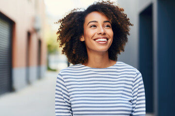 A woman with curly hair wearing a striped shirt smiles warmly.
