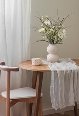 The beautiful interior of the living room - round wooden table with a muslin tablecloth, a vase...