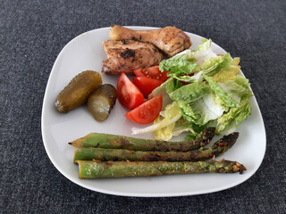 Homemade grilled chicken legs with grilled asparagus, green salad,  sliced tomatonand cucumber picklesy.