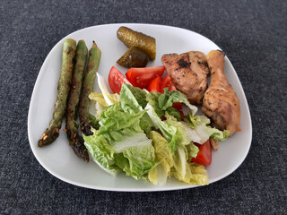 Homemade grilled chicken legs with grilled asparagus, green salad,  sliced tomatonand cucumber picklesy.