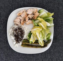Homemade grilled chicken with rice and grilled asparagus, served on a white plate. Brocolli seeds on top of the rice