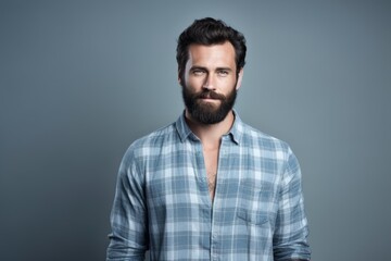 Obraz premium A man with a beard confidently stands in front of a plain gray background.