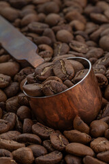 Hand-roasted Arabica Maragogipe coffee beans in a copper measuring spoon resting on top of the...