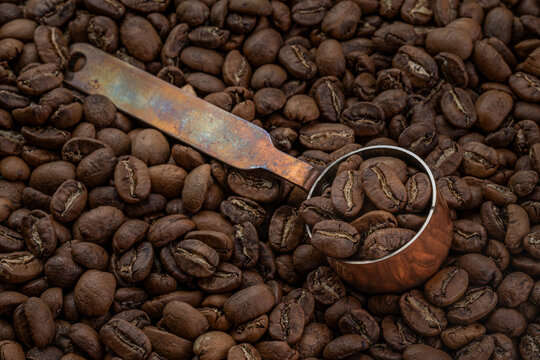Hand-roasted Arabica Maragogipe coffee beans in a copper measuring spoon resting on top of the freshly roasted beans.